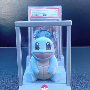 May include: A blue and white Squirtle Pokemon figure is displayed in a clear acrylic case with a gray base. The figure is sitting on a gray base with a red and white Pokemon logo. The figure is in a graded card case with a PSA label that reads "2024 Pokemon SGC EN Squirtle Illustration Rare #143 MINT 10 102279843".
