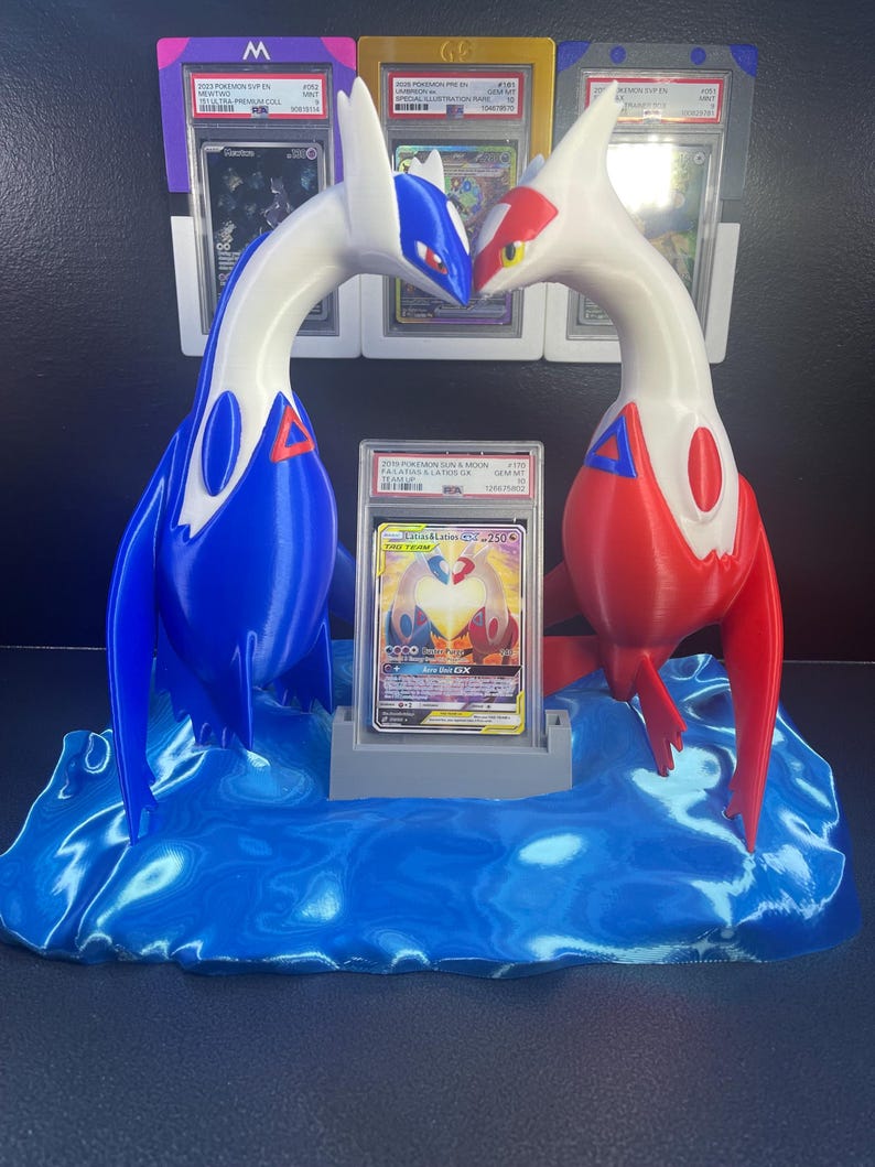 Puede incluir: Una pantalla impresa en 3D con dos figuras de drag&oacute;n estilizadas, una azul y blanca, la otra roja y blanca, enfrentadas. Una tarjeta comercial clasificada se muestra entre ellas, colocada sobre una base de onda azul. Se ven tarjetas clasificadas adicionales en el fondo.