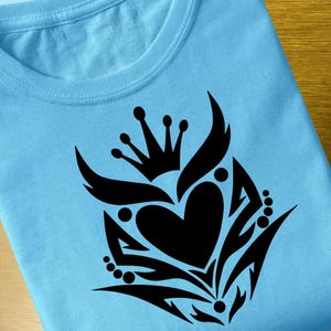 May include: A blue t-shirt with a black design of a stylized heart with a crown and floral elements.