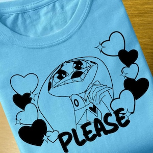 May include: A light blue t-shirt with a black and white illustration of a cartoon character with the text "PLEASE" printed on the shirt.