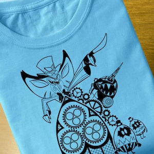 May include: A light blue t-shirt with a black and white graphic print of a cartoon character with wings and a top hat. The character is holding a gear and is surrounded by other gears. There are also two smaller cartoon characters in the bottom right corner.