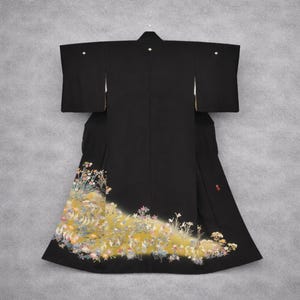 May include: A black kimono with a floral design on the lower portion. The kimono has a yellow and white floral pattern with pink and green accents. The sleeves are wide and the garment is hanging on a hanger.