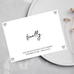 May include: A white card with black text that says "finally." and "SAVE THE DATE FOR SAM & CATHY'S WEDDING SEPTEMBER 20, 2026 - YARRA VALLEY". There are small hearts drawn around the text.