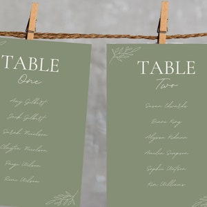 May include: Two green cards with white text and floral designs. The first card says "TABLE One" and lists names. The second card says "TABLE Two" and lists names.