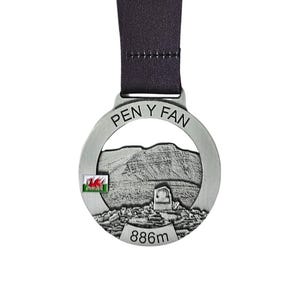 Könnte beinhalten: Silberfarbene Medaille mit schwarzem Band. Sie zeigt den Schriftzug "PEN Y FAN" und eine Berglandschaft. Die walisische Flagge ist zu sehen, und die Medaille trägt die Angabe "886m".