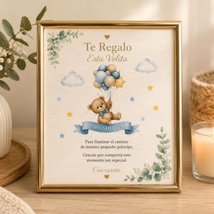Peut inclure: Une impression encadrée en or représentant un ours en peluche brun tenant un bouquet de ballons bleus, beiges et jaunes. Le texte indique Te Regalo Esta Velita, Baby Shower et des phrases en espagnol. Le design inclut des nuages, des étoiles et du feuillage.