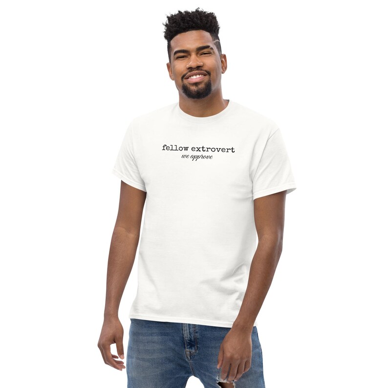 May include: A white short-sleeved t-shirt featuring the black text "fellow extrovert" in a typewriter-style font on the top line and "we approve" in a cursive script font on the second line, centered on the chest area of the garment.