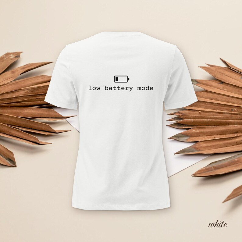 May include: A white short-sleeved t-shirt featuring a black graphic of an empty battery icon centered above the text "low battery mode" in a simple sans-serif font. The shirt has a crew neckline and a standard fit, presented in a clean style.