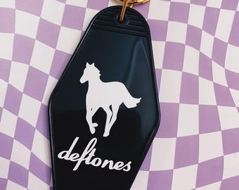 May include: Black motel key chain with a white silhouette of a horse and the word "Deftones" in white lettering.