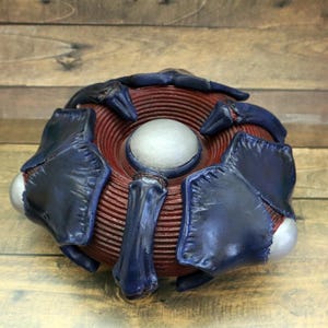 Puede incluir: Un objeto decorativo rojo y azul con un centro circular y múltiples brazos. El objeto tiene una superficie texturizada y un centro plateado.