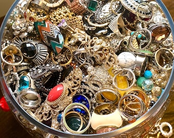 May include: A glass bowl filled with a variety of rings, including gold, silver, and gemstone rings. The rings are of different styles and sizes, and some have intricate designs.
