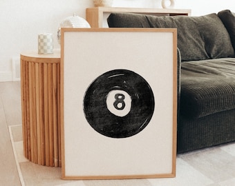 May include: A framed black and white print of a black eight ball with a white outline. The print is hanging on a wall in a living room with a couch and a side table.