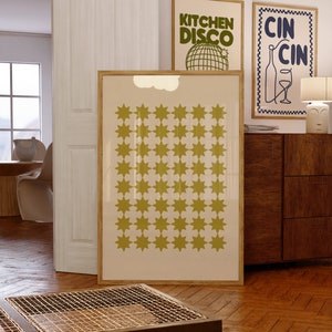 May include: A framed print with a beige background and a pattern of 42 yellow stars. The print is hanging on a wall with two other framed prints above it. The print on the left says "Kitchen Disco" and the print on the right says "Cin Cin".