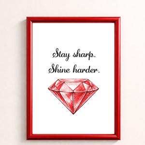 Könnte beinhalten: Ein gerahmter Druck mit rotem Rahmen. Der Druck zeigt den Text "Stay sharp. Shine harder." über einer roten Diamantenillustration. Der Diamant ist schattiert, um ihm Tiefe zu verleihen. Der Hintergrund ist weiß.