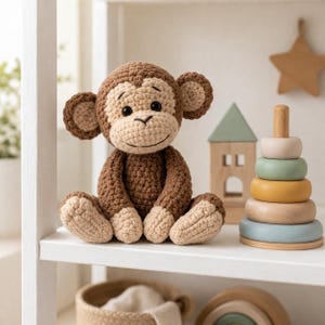 May include: A handmade crochet monkey doll in shades of brown and beige sits on a white shelf. The monkey has a smiling face, large ears, and is seated with its legs extended. Other wooden toys, including a star and a stacking ring toy, are also on the shelf.