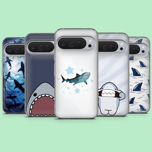 May include: A collection of five phone cases with shark-themed designs. The cases feature various shark illustrations, including a shark in the ocean, a shark with an open mouth, and shark fins. The cases are in clear and navy blue.