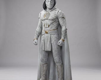 Op de afbeelding: Een wit kostuum voor het hele lichaam met een capuchonmasker met gewikkelde stoftexturen, een borstembleem met een halve maan, een goudkleurige riemgesp en een lange cape. Het pak is gedetailleerd met ingewikkelde patronen en stofstroken.