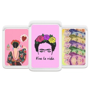 May include: Three rectangular protective cases featuring artistic illustrations of Frida Kahlo. The left case shows a back view with a heart icon, the center case displays a portrait with the text Viva la vida, and the right case shows a repeating face pattern.