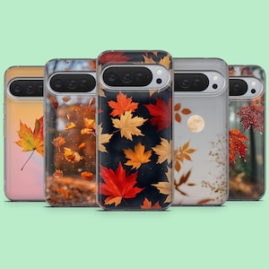May include: Five smartphone cases arranged in a row, each featuring a distinct autumn-themed design. The patterns include falling maple leaves in shades of red, orange, and yellow, a full moon, and forest scenes, all with a horizontal camera cutout.