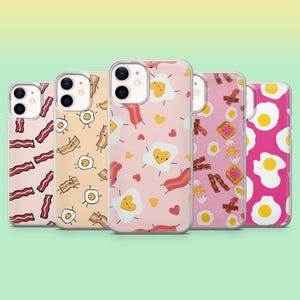 Könnte beinhalten: Fünf Handyhüllen mit Frühstücksmotiven. Die Hüllen zeigen Muster aus Speck, Spiegeleiern und Toast auf rosa-, pfirsich- und magentafarbenem Hintergrund. Jede Hülle hat einen transparenten Rand und ein glänzendes Finish.