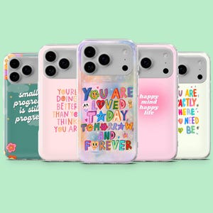 May include: Five phone cases with uplifting messages and vibrant designs. The cases display phrases such as "You are loved" and "Small progress is still progress" in diverse fonts and colours. The cases have a clear, protective design.