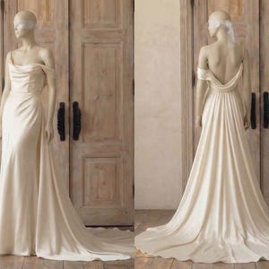 A mannequin wearing a long, off-the-shoulder white wedding dress with a flowing train, displayed in front of a wooden door.