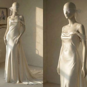 A mannequin wearing a long, flowing white wedding dress with a train, standing in a room with a vase of dried flowers and a window.