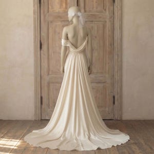 A mannequin wearing a long, flowing white wedding dress with a train, standing in front of a wooden door.