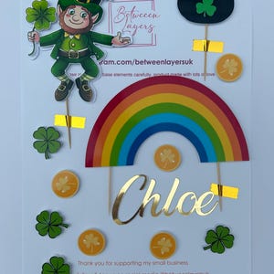 May include: A selection of St. Patrick's Day cake toppers featuring a leprechaun, rainbow, pot of gold, shamrocks, and gold coins. The name "Chloe" is written in gold script. Text includes "Between Layers" and "Thank you for supporting my small business."