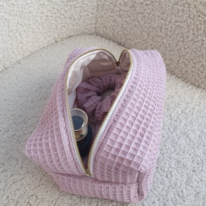 Close-up of the zipper pull on the eco-friendly makeup bag, highlighting its stylish and functional design. High-quality golden metal zipper closure detail on the eco-conscious waffle makeup bag, showcasing secure design.