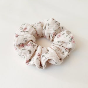 Puede incluir: Un scrunchie blanco con un patrón floral con pequeñas flores rosas y hojas verdes.