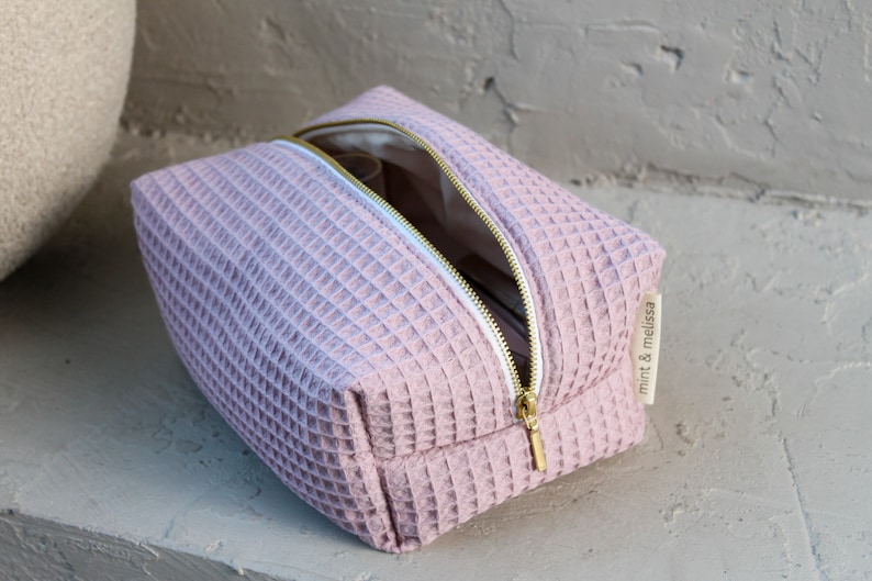 Side view of the sustainable makeup bag, illustrating its slim profile and minimalist design. High-quality  gold metal zipper closure detail on the eco-conscious waffle makeup bag, showcasing secure design.