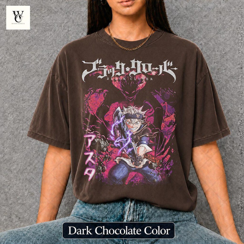 Może przedstawiać: Ciemnobrązowy t-shirt z grafiką z anime Black Clover. Projekt zawiera japoński tekst i żywą ilustrację postaci z mieczem i fioletową energią. Koszulka ma wygląd vintage.