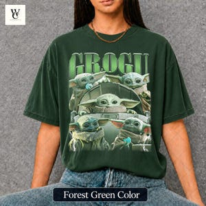 May include: Forest green t-shirt featuring a graphic of Grogu from The Mandalorian. The design includes multiple images of Grogu, with the name "GROGU" in green block letters above. The shirt is a dark green color.