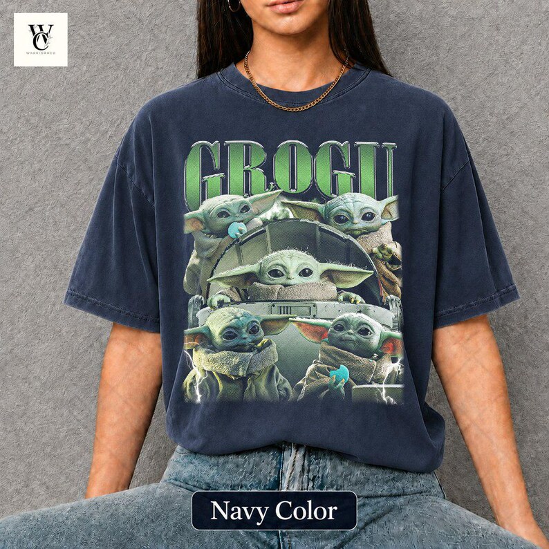 May include: Navy blue t-shirt featuring a graphic of Grogu, also known as Baby Yoda, from The Mandalorian. The design includes multiple images of Grogu in a pod, with the word "GROGU" in green above. The shirt is labeled "Navy Color".