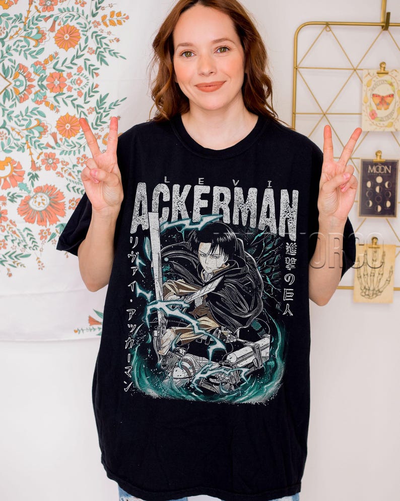 Pu&ograve; includere: T-shirt nera con grafica che presenta il nome "Levi Ackerman" in lettere bianche invecchiate. Il design include un'illustrazione di un personaggio con una spada, testo giapponese e uno sfondo turchese e bianco.