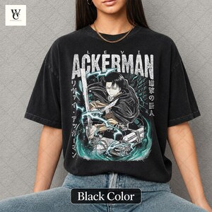 Pu&ograve; includere: T-shirt nero con grafica bianca "LEVI ACKERMAN" e illustrazione di un personaggio. Il design include testo giapponese e un effetto energetico turchese e bianco. La maglietta &egrave; di un nero scuro sbiadito.