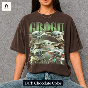 May include: Dark chocolate-colored t-shirt featuring a graphic of Grogu, also known as Baby Yoda, with the word "GROGU" in green block letters. The design includes multiple images of Grogu. The shirt is a relaxed fit.