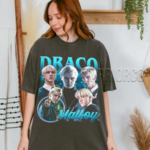 Könnte beinhalten: Dunkelgraues T-Shirt mit einer Grafik von Draco Malfoy aus der Harry-Potter-Reihe. Das Design enthält den Namen "Draco" in Blau und den Namen "Malfoy" in Schreibschrift, zusammen mit mehreren Bildern der Figur.