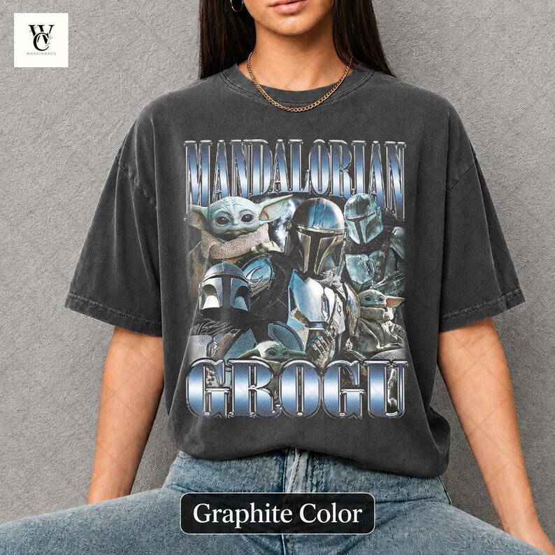 May include: Graphite-colored t-shirt featuring a graphic of characters from The Mandalorian series, including Grogu and Mandalorian figures. The text "MANDALORIAN" and "GROGU" are displayed in a metallic blue font.