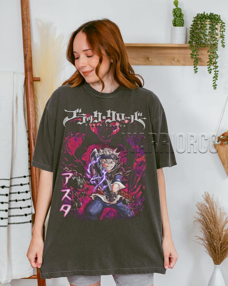 Może przedstawiać: Ciemnoszara koszulka z grafiką postaci z anime z fioletowymi efektami energetycznymi. Koszulka ma japoński tekst na g&oacute;rze i imię postaci po japońsku po lewej stronie. Koszulka jest noszona przez osobę.