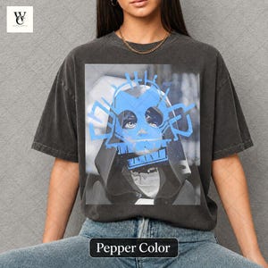 Könnte beinhalten: Dunkelgraues T-Shirt mit blauem Grafikdesign. Die Grafik zeigt ein Gesicht mit blauen Akzenten und den Text "Pepper Color" unten. Das T-Shirt hat eine lockere Passform.