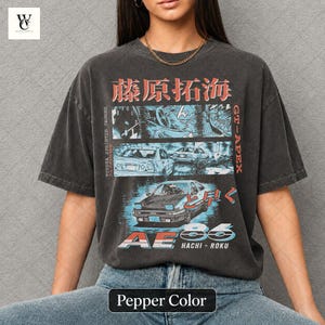 Könnte beinhalten: Pfefferfarbenes T-Shirt mit einem grafischen Design mit japanischem Text und Illustrationen eines Autos. Das Design enthält den Text "TOYOTA SPRINTER TRUENO" und "GT-APEX". Das Shirt hat auch den Text "AE86 HACHI-ROKU".