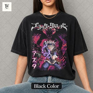 Może przedstawiać: Czarny t-shirt z grafiką z anime Black Clover. Projekt zawiera japoński tekst i ilustrację postaci z fioletowymi i r&oacute;żowymi akcentami. Koszulka ma wygląd vintage.