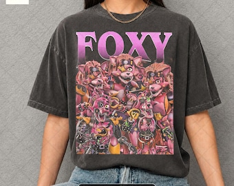 May include: Dark gray t-shirt with the word "FOXY" in pink and a graphic of several cartoon fox characters. The shirt is a pepper color and has a vintage look.