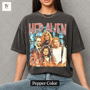 以下が含まれることがあります： HED ALIENのバンドグラフィックがプリントされたペッパーカラーのTシャツ。カラフルなデザインにはバンドメンバーと炎が描かれています。Tシャツは濃いグレー色です。