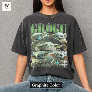 May include: Graphite-colored t-shirt featuring a graphic of Grogu from The Mandalorian. The design includes multiple Grogu characters in a vehicle, with the name "GROGU" in green block letters above. The shirt is a relaxed fit.