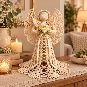 May include: A crocheted angel figurine in a light beige yarn, featuring an intricate openwork pattern on the wings and dress. The figure has a halo of white pearls, holds a small bouquet of cream and yellow roses, and is accented with a ribbon.