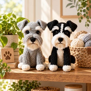 May include: Two handmade crochet Schnauzer dog figurines sitting side by side. One dog is light gray with white accents on the face and paws, while the other is black with a white chest, face stripe, and paws. Both feature black noses and eyes.