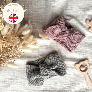 Könnte beinhalten: Zwei gestrickte Baby-Stirnbänder in Staubrosa und Grau mit Schleifendetail. Ein Elefant und eine Rassel aus Holz liegen neben den Stirnbändern. Ein Strauß Trockenblumen und der Text "PDF Pattern English" sind ebenfalls im Bild.